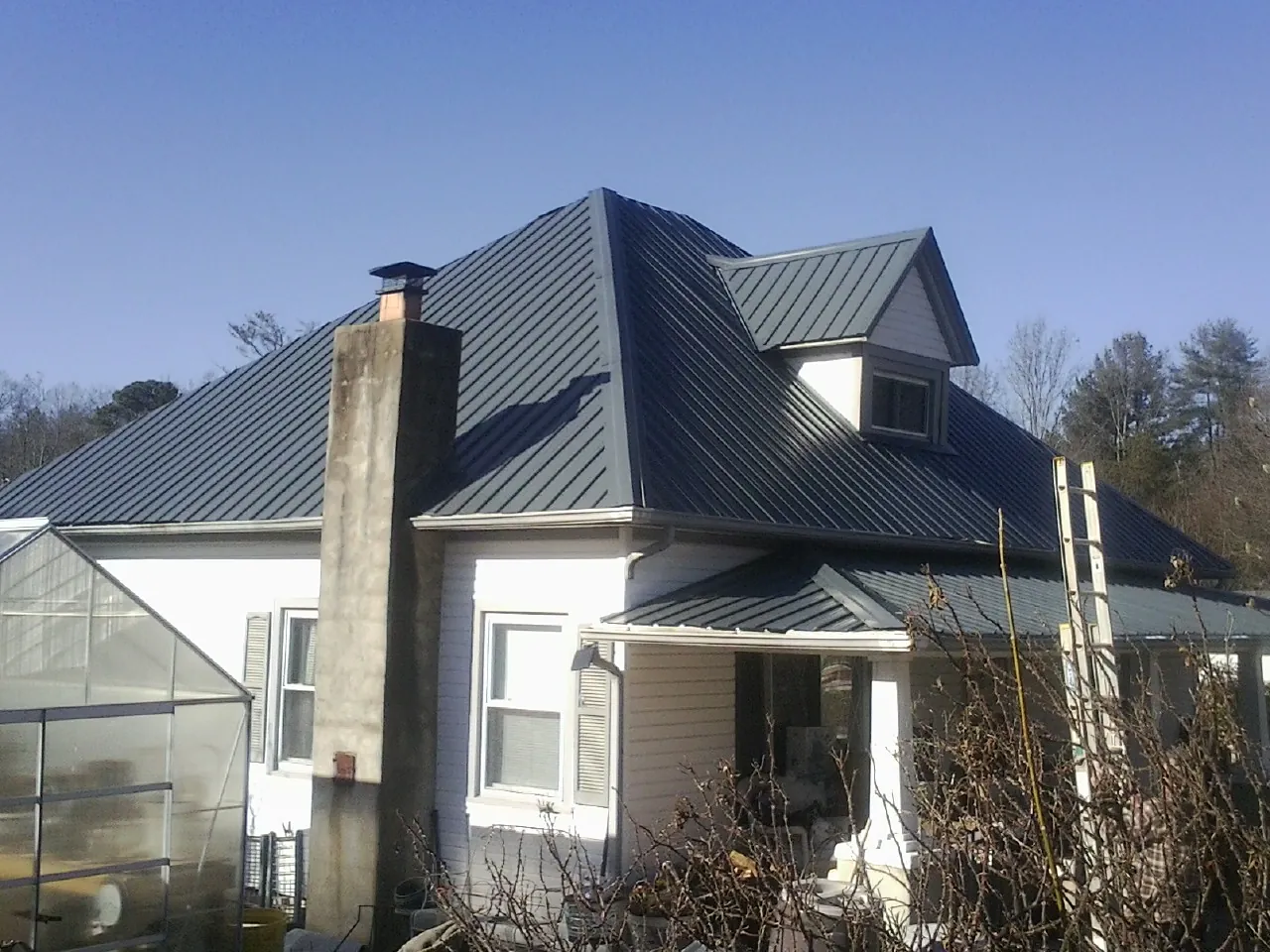 Dark blue standing seam metal roof on a white farmhouse with dormer — Slate & Tile Roof Repair by Roofing Brothers in New Woodstock