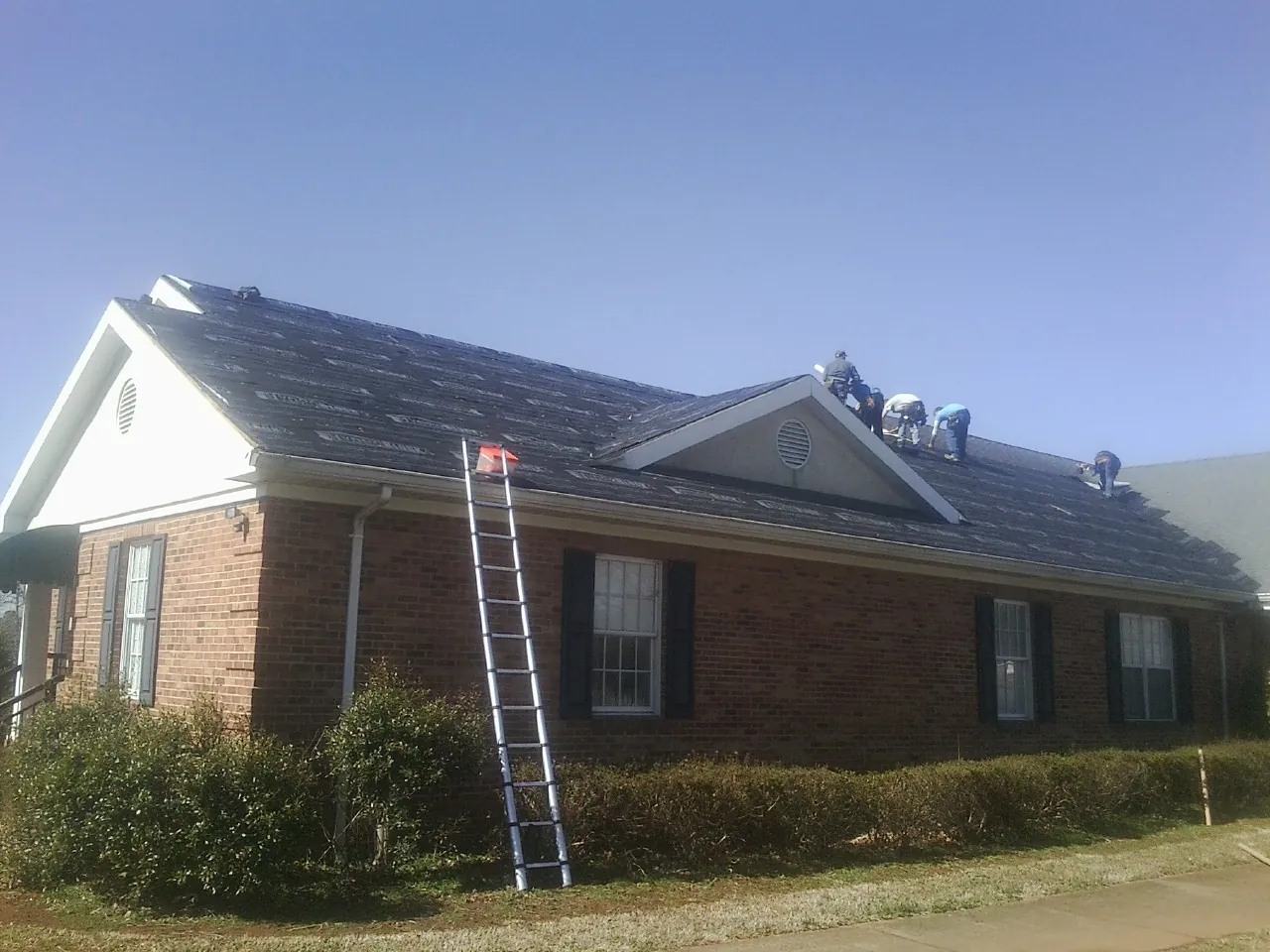 Crew tearing shingles off a brick ranch roof with a ladder set — Emergency Roof Repair work by our crew in New Woodstock