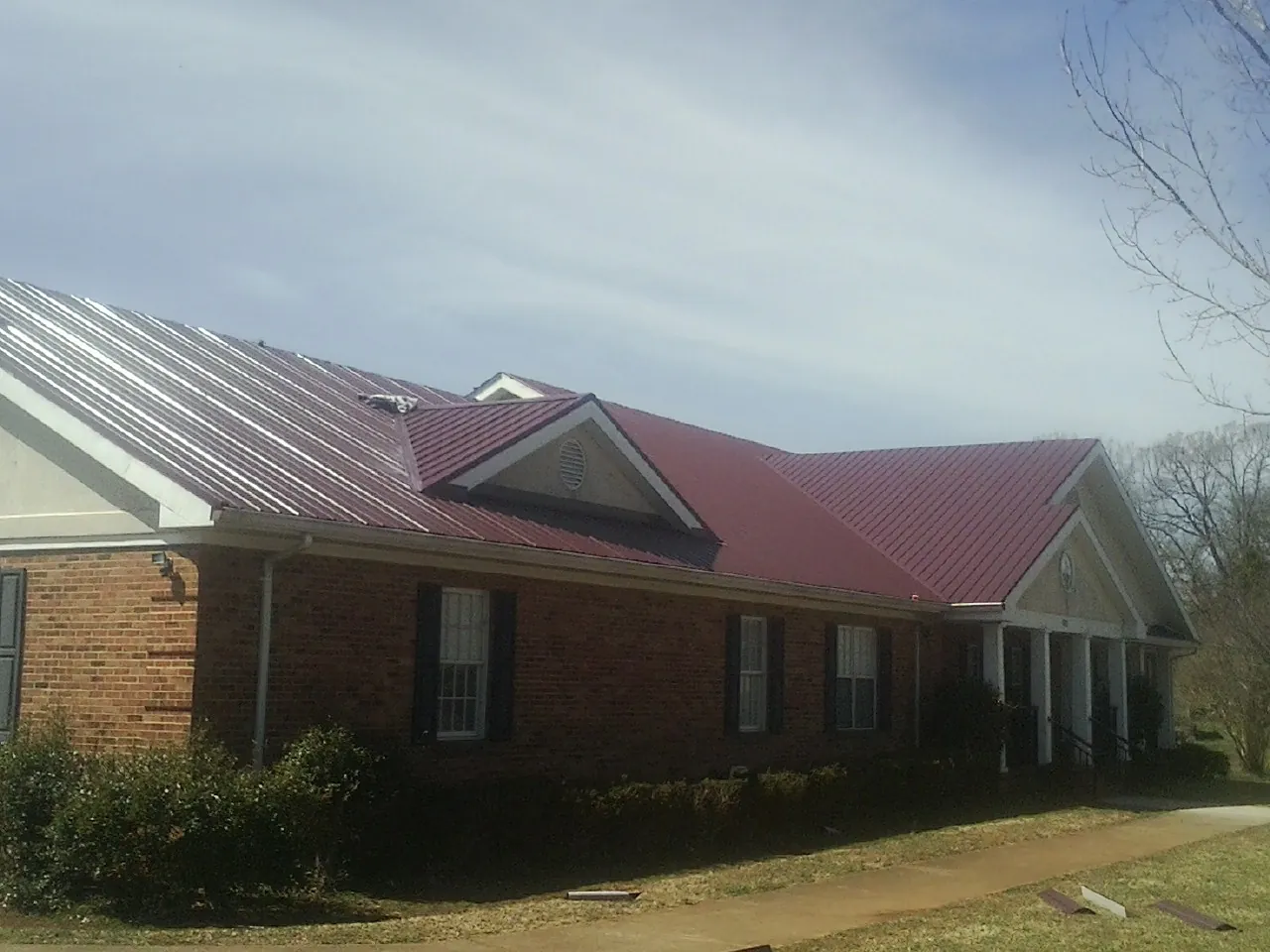 Red metal roof with gabled entries on a long brick building, from a Hail Damage Roof Repair job in New Woodstock