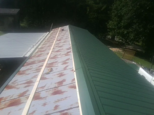 Old rusted panels beside newly installed green metal roofing — Wind Damage Roof Repair by Roofing Brothers in New Woodstock