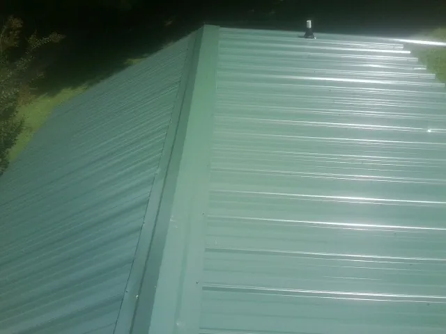 New green metal panels meeting at the ridge of a roof — Flat Roof Repair work by our crew in New Woodstock