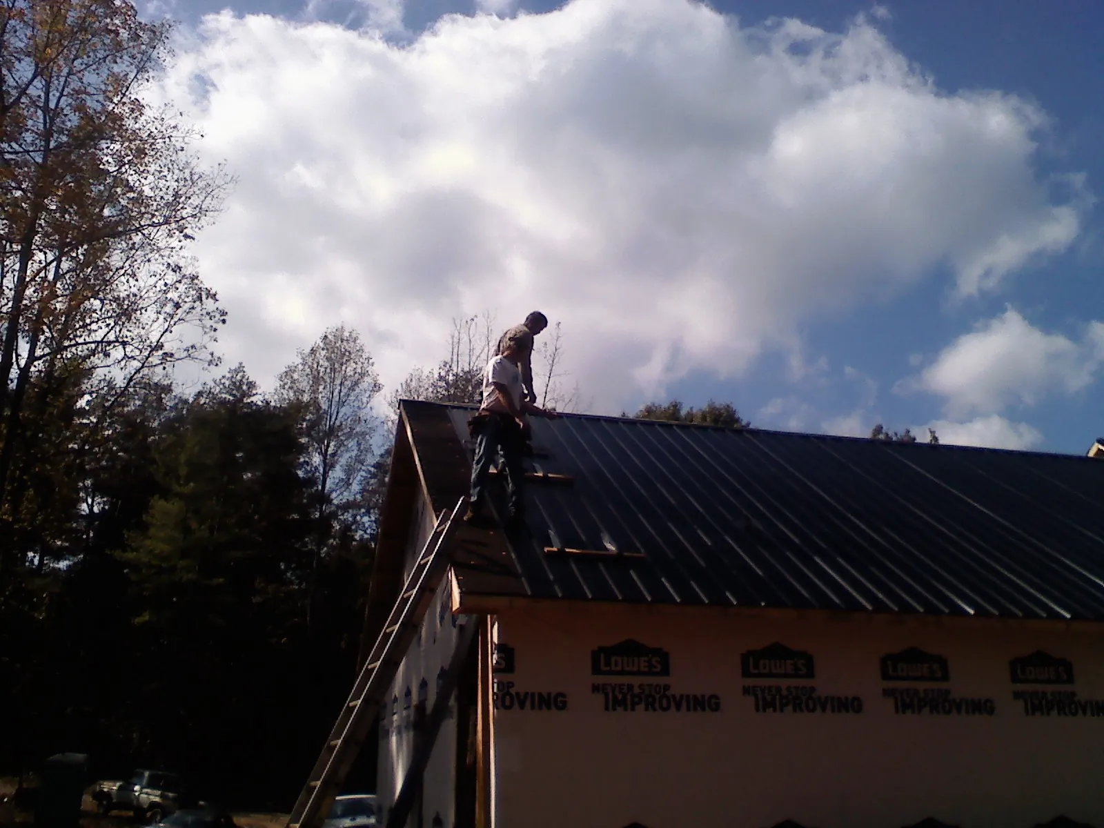 Roofer fastening dark metal panels high against a cloudy sky, from a Roof Inspection job in New Woodstock