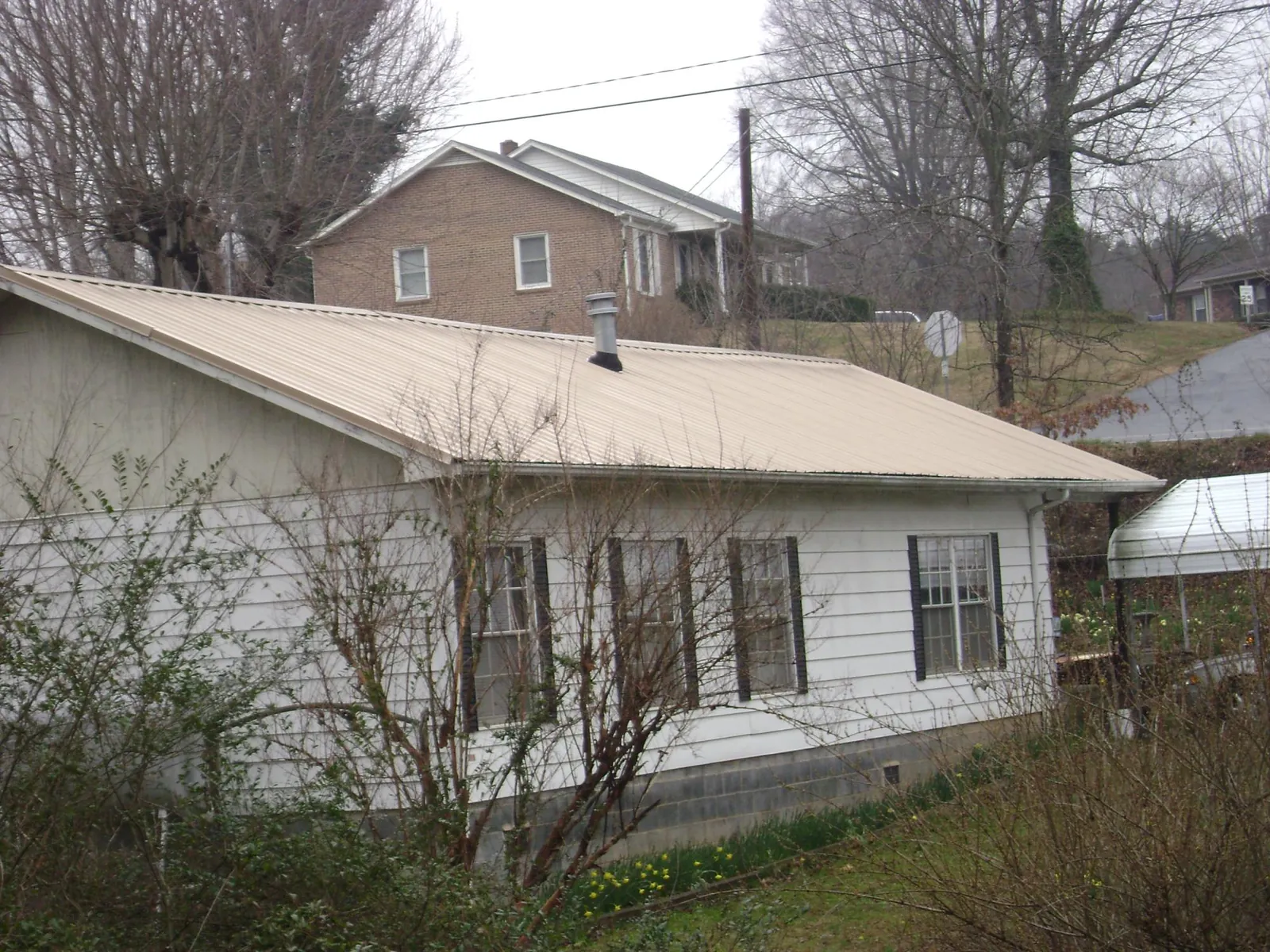Tan metal roof on a white sided house set into a hillside — Commercial Roofing by Roofing Brothers in New Woodstock