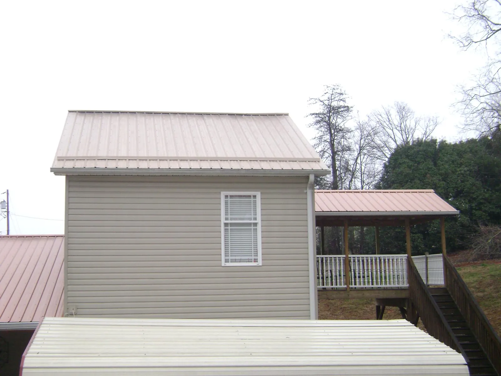 Tan metal roofs on a two story addition and attached porch, from a Roof Replacement job in New Woodstock